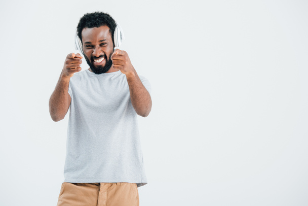 aufgeregter afrikanisch-amerikanischer Mann, der mit Kopfhörern Musik zeigt und hört, isoliert auf grau - Foto, Bild