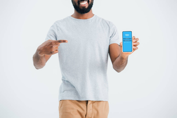 KYIV, UKRAINE - MAY 17, 2019: cropped view of african american man pointing at smartphone with skype app, isolated on grey  - Foto, Bild
