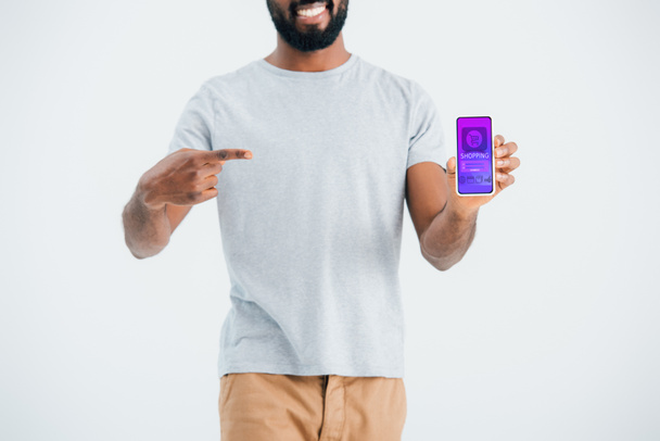 KYIV, UCRANIA - 17 de mayo de 2019: Vista recortada del hombre afroamericano apuntando al teléfono inteligente con la aplicación de compras, aislado en gris
 - Foto, Imagen