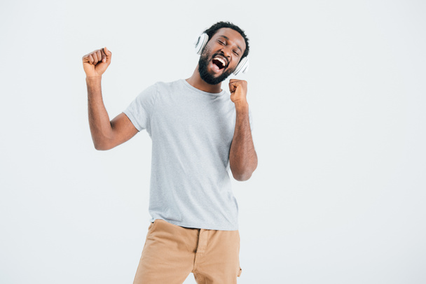 excited african american man singing and listening music with headphones, isolated on grey - Foto, imagen