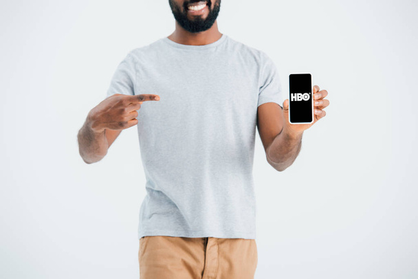 KYIV, UCRANIA - 17 de mayo de 2019: vista recortada del hombre afroamericano apuntando al teléfono inteligente con la aplicación HBO, aislado en gris
  - Foto, Imagen