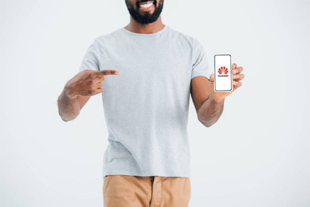 Κίεβο, Ουκρανία-17 Μαΐου, 2019: περικομμένη όψη του αφρικανικού αμερικανικού ανθρώπου που δείχνει στο smartphone με την εφαρμογή Huawei, απομονώνεται σε γκρι  - Φωτογραφία, εικόνα