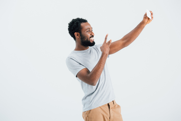 African American man met overwinning teken nemen selfie op smartphone, geïsoleerd op grijs  - Foto, afbeelding