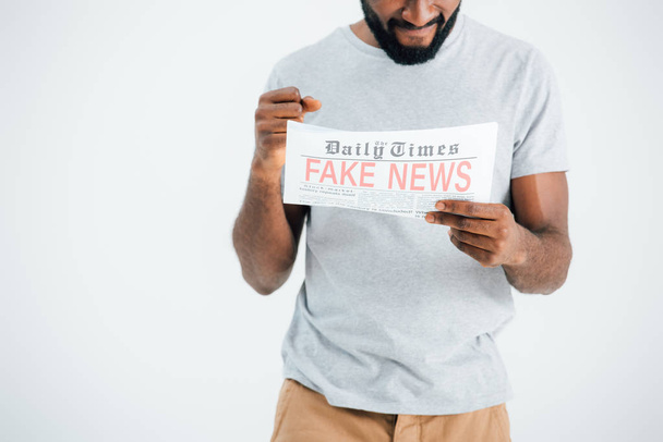 cropped view of confused african american man reading newspaper with fake news isolated on grey - Foto, Imagen