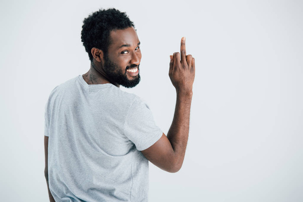 smiling african american man in grey t-shirt showing middle finger isolated on grey - Foto, immagini