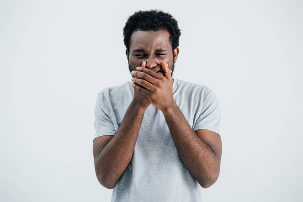 handsome emotional african american man in grey t-shirt closing mouth isolated on grey - 写真・画像