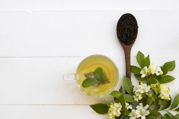 pflanzliche gesunde Getränke heißer grüner Tee mit püriertem Blatttee in Holzlöffel und Blütenjasmin für entspanntes Lifestyle-Arrangement flacher Liegestil auf weißem Hintergrund  - Foto, Bild