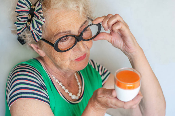 Mujer hipster arrugado maduro en gafas divertidas examina un frasco de crema facial. El cuidado de la piel para las mujeres 60-70 años. Mujeres Salud
 - Foto, Imagen