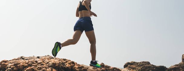 Woman running to rocky mountain top at seaside - 写真・画像