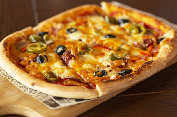 Pizza with jalapeno chillies and olives on wooden pizza board, selective focus. - Photo, Image