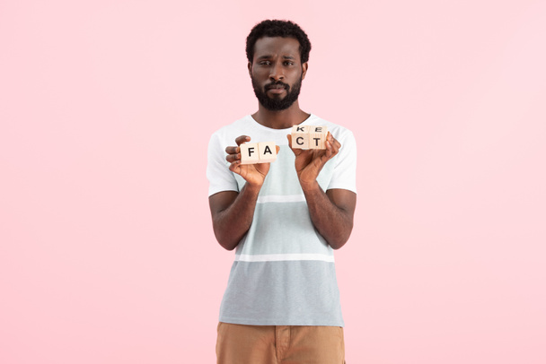 african american man holding alphabet cubes with fact word, isolated on pink - Foto, imagen