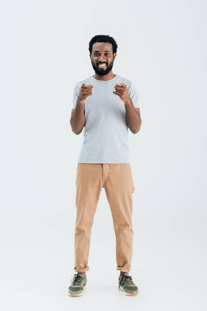 smiling african american man in grey t-shirt pointing isolated on grey - Foto, immagini