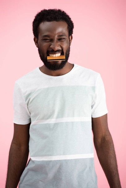 joyeux homme afro-américain mordre carte de crédit isolé sur rose
 - Photo, image