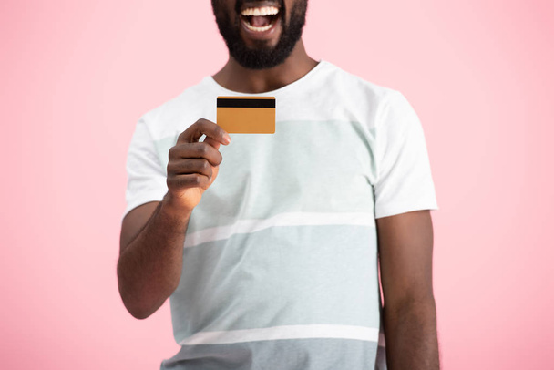 vista recortada de hombre afroamericano emocionado mostrando tarjeta de crédito aislado en rosa
 - Foto, Imagen