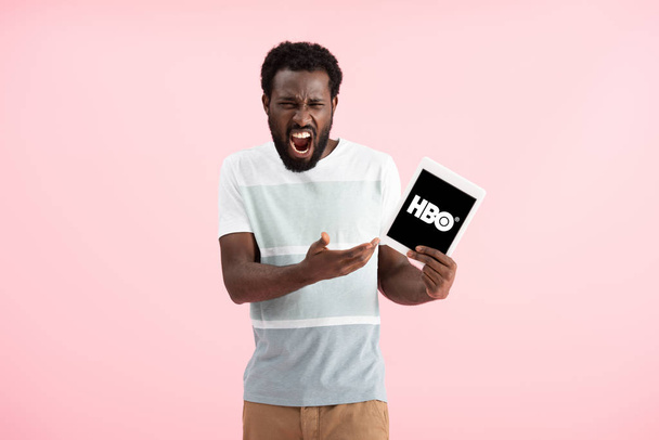 KYIV, UKRAINE - MAY 17, 2019: emotional african american man shouting and showing digital tablet with HBO app, isolated on pink - Photo, image