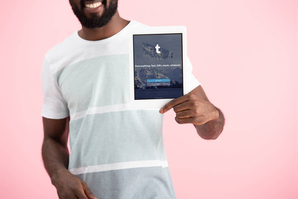 KYIV, UCRANIA - 17 DE MAYO DE 2019: vista recortada del hombre afroamericano mostrando tableta digital con aplicación tumblr, aislado en rosa
 - Foto, imagen