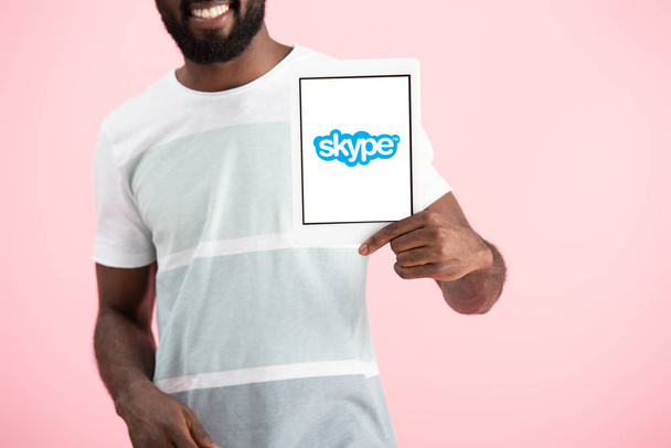 KYIV, UKRAINE - MAY 17, 2019: cropped view of african american man showing digital tablet with skype app, isolated on pink - Fotó, kép