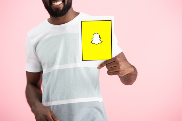 KYIV, UKRAINE - MAY 17, 2019: cropped view of african american man showing digital tablet with Snapchat app, isolated on pink - Fotó, kép