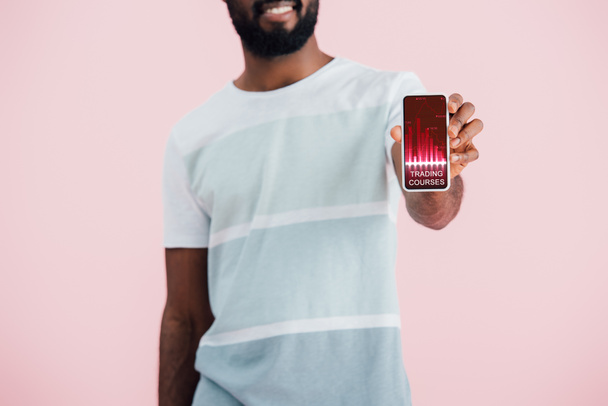 貿易コースアプリでスマートフォンを示すアフリカ系アメリカ人男性のトリミングビュー, ピンクに隔離  - 写真・画像
