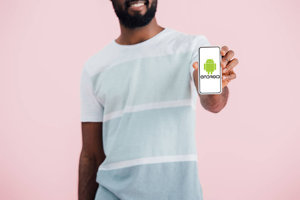 KYIV, UKRAINE - MAY 17, 2019: cropped view of african american man showing smartphone with android app, isolated on pink  - Fotoğraf, Görsel