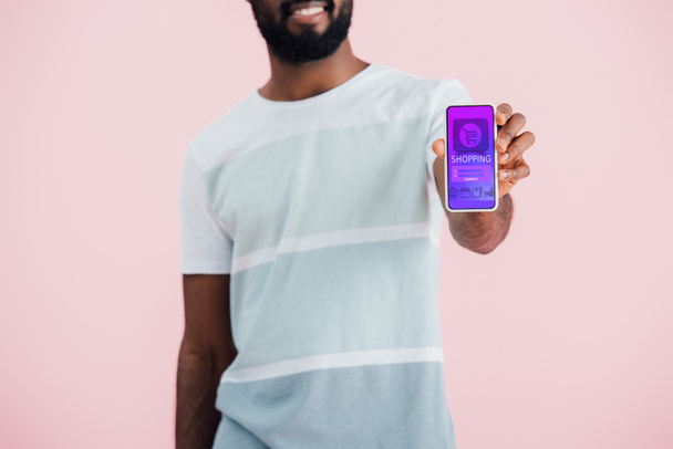 vista ritagliata dell'uomo afroamericano che mostra smartphone con app per lo shopping, isolato su rosa
  - Foto, immagini