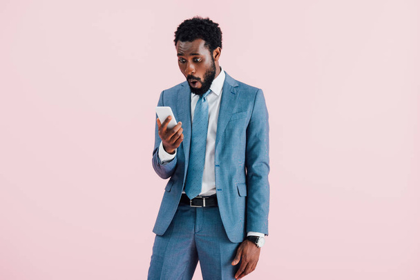 surprised african american businessman using smartphone, isolated on pink   - Foto, immagini