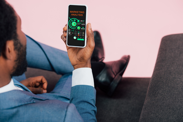 η περικομμένη θέα του αφρικανικού Αμερικανού επιχειρηματία που δείχνει smartphone με ανάλυση μάρκετινγκ, απομονωμένη σε ροζ - Φωτογραφία, εικόνα