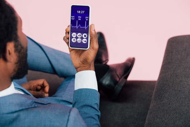 cropped view of african american businessman showing smartphone with health app, isolated on pink - Photo, Image