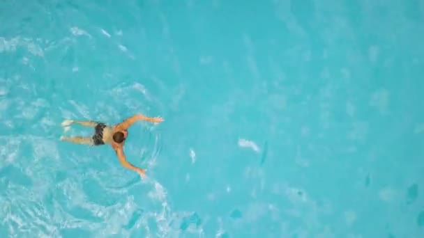 Young man swimming in floating pool aerial view. View from above flying drone male swimmer in swimming pool. Water sport. Summer activity. - Video, Çekim