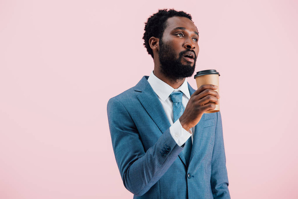 tired african american businessman holding coffee to go, isolated on pink - Foto, Imagem