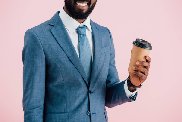 nyírt kilátás mosolygó afro-amerikai üzletember a gazdaság kávét menni, izolált rózsaszín - Fotó, kép