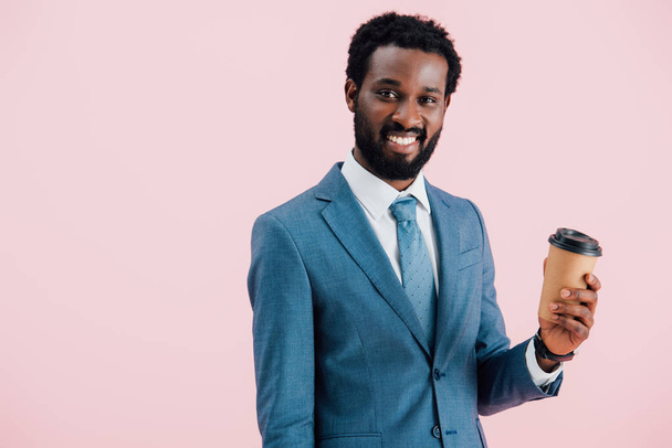 feliz empresário afro-americano segurando café para ir, isolado em rosa
 - Foto, Imagem