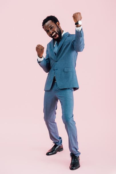 スーツを着て興奮した成功したアフリカ系アメリカ人のビジネスマン、ピンクで孤立 - 写真・画像
