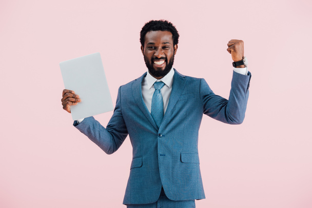 excited african american businessman in suit holding laptop isolated on pink - Foto, Imagem