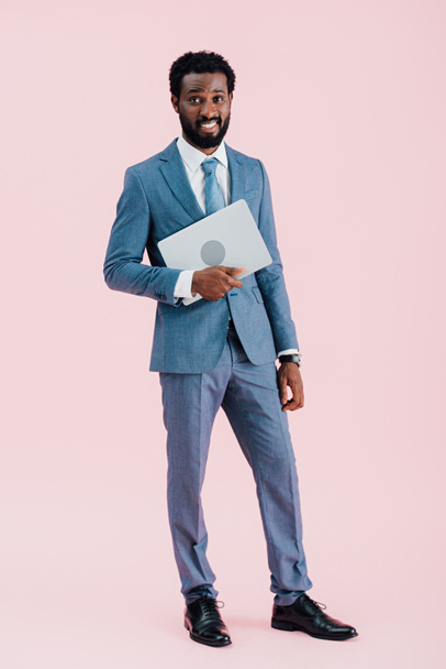 african american businessman holding laptop isolated on pink - Fotó, kép