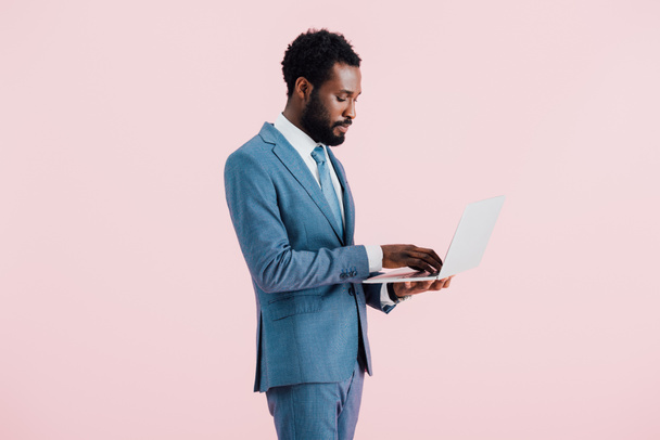 african american businessman using laptop isolated on pink - Foto, imagen