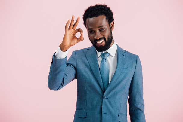 sorridente empresário afro-americano em terno mostrando sinal ok, isolado em rosa
 - Foto, Imagem