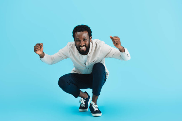 excited bearded african american man sitting isolated on blue - Photo, Image