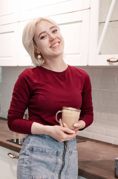Young happy gitl drinking coffee on kitchen at home in morning. - Photo, image
