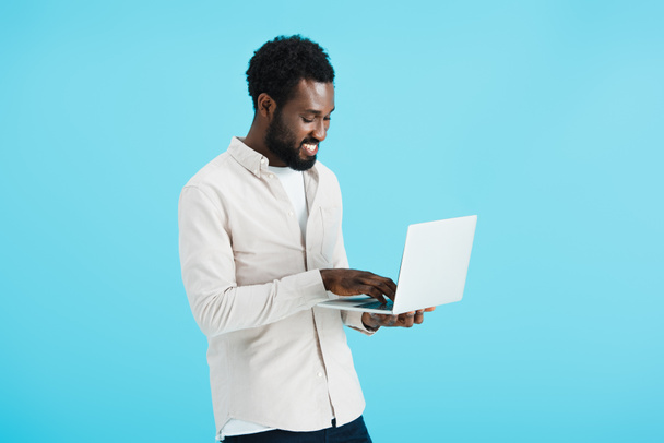 smiling african american man in white shirt using laptop isolated on blue - Foto, Imagen