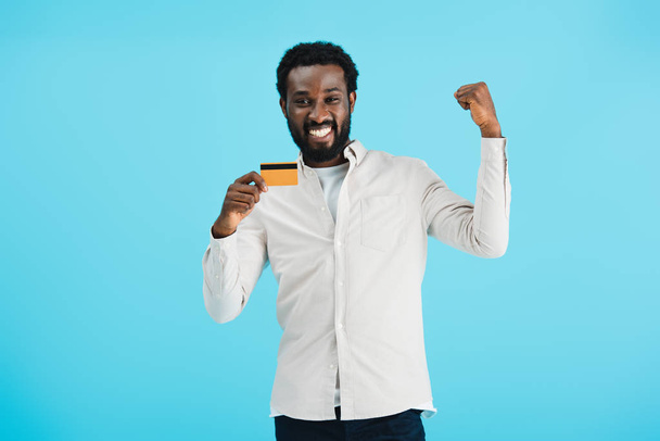 hombre afroamericano emocionado mostrando tarjeta de crédito aislado en azul
 - Foto, Imagen