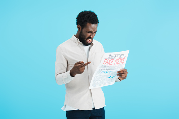 agresivní Afroameričan čte noviny s falešnými zprávami a ukazuje prostředníček izolovaný na modrém - Fotografie, Obrázek
