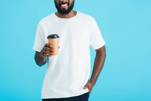 abgeschnittene Ansicht eines lächelnden afrikanisch-amerikanischen Mannes mit Coffee to go, isoliert auf blau - Foto, Bild