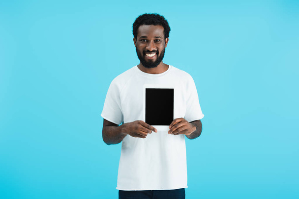 Gelukkig African American man toont digitale tablet met blanco scherm geïsoleerd op blauw  - Foto, afbeelding