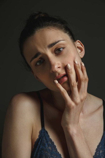 Half-length portrait of young sad woman on dark studio background - Fotó, kép