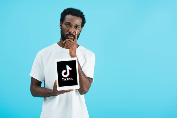 KYIV, UCRAINA - 17 MAGGIO 2019: uomo afroamericano riflessivo che mostra tablet digitale con app Tik Tok, isolato sul blu
 - Foto, immagini