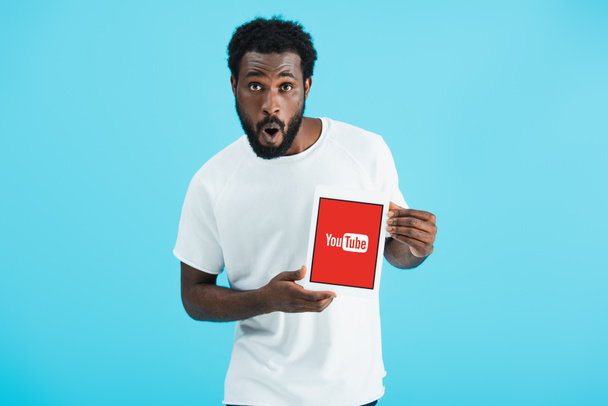 KYIV, UCRAINA - 17 MAGGIO 2019: sorpreso uomo afroamericano che mostra tablet digitale con app youtube, isolato su blu
 - Foto, immagini