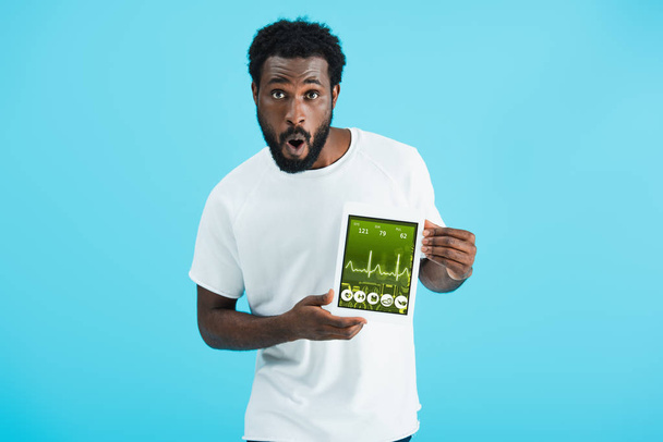 shocked african american man showing digital tablet with health app, isolated on blue - Photo, Image