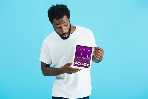 šokoval africký americký muž zobrazující digitální tablet se zdravotnickým App, izolovaný na modrém - Fotografie, Obrázek