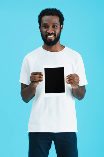 χαμογελαστός Αφρικανός Αμερικανός άνθρωπος δείχνοντας ψηφιακό δισκίο με κενή οθόνη απομονωμένη στο μπλε  - Φωτογραφία, εικόνα